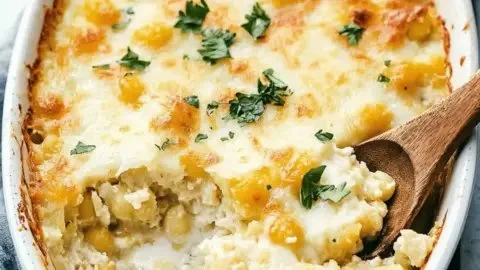 Cheesy hominy casserole served in a baking dish with toppings.