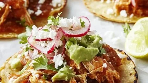 Plate of Chicken Tinga Tostadas topped with avocado and fresh salsa