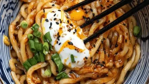 Bowl of homemade Chili Garlic Udon Noodles topped with fresh herbs and spicy sauce.