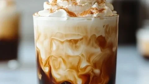 Glass of creamy cold brew coffee with a frothy top and coffee beans.