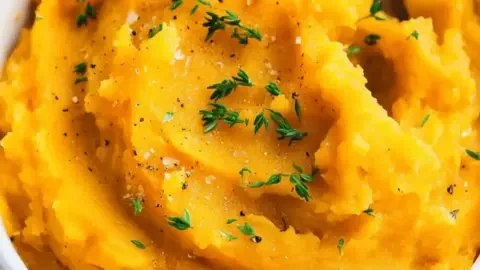 Creamy mashed butternut squash in a bowl with a sprinkle of herbs