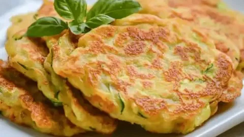 Crispy zucchini blossom pancakes served on a plate with fresh herbs.