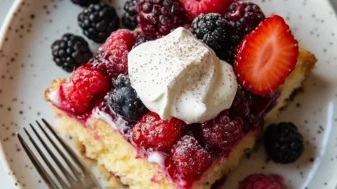 Sliced easy berry sheet cake topped with fresh berries and whipped cream
