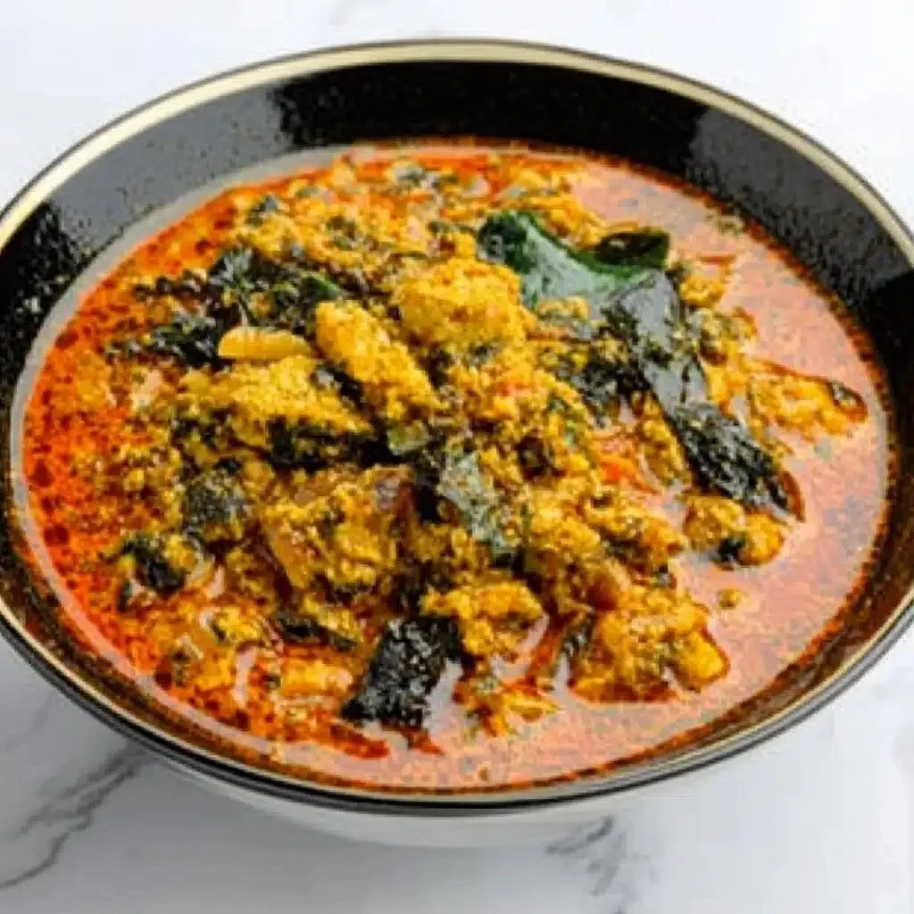 A bowl of Egusi Soup garnished with vegetables and served with fufu.