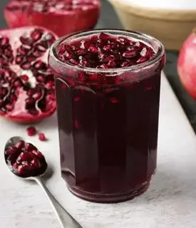 Jar of homemade pomegranate jelly with fresh pomegranates