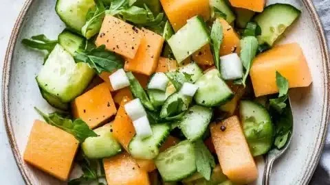 A refreshing cucumber melon salad served in a bowl, garnished with mint leaves.